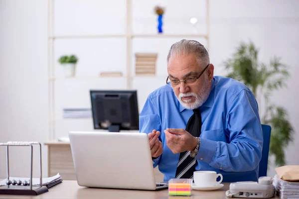 Oude mannelijke werknemer die op kantoor werkt — Stockfoto