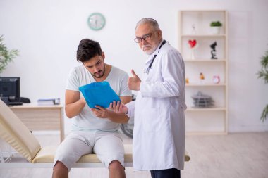 Genç erkek hasta yaşlı erkek doktoru ziyaret ediyor.