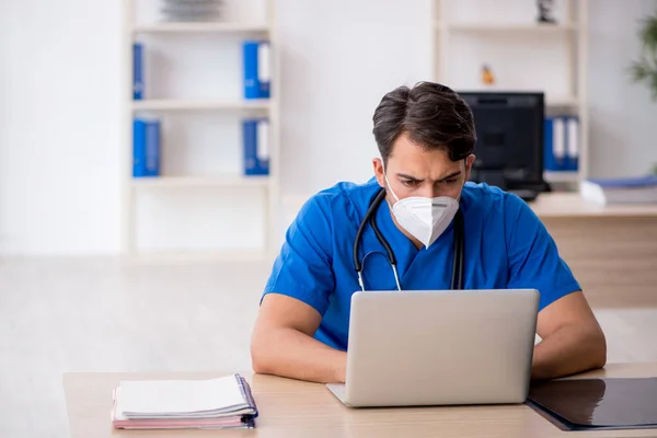 Jonge mannelijke arts werkzaam in de kliniek tijdens pandemie — Stockfoto