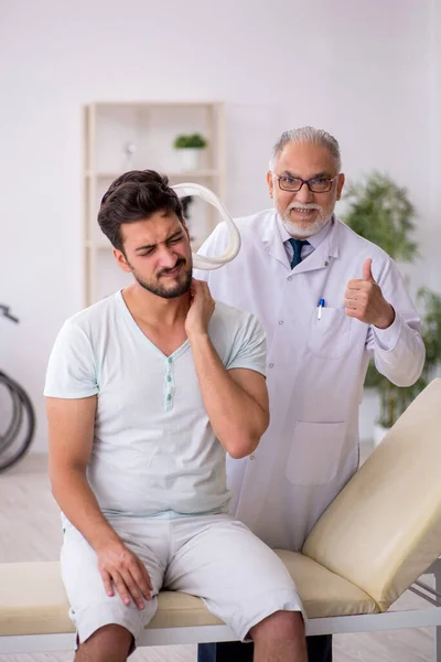 Genç boynu yaralı erkek hasta yaşlı erkek doktoru ziyaret ediyor. — Stok fotoğraf