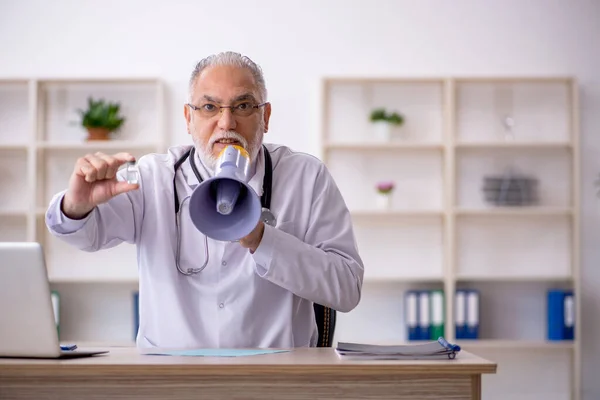 Velho médico masculino segurando megafone na clínica — Fotografia de Stock