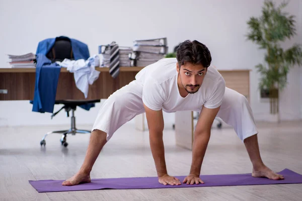 Joven empleado masculino haciendo ejercicios deportivos en la oficina — Foto de Stock