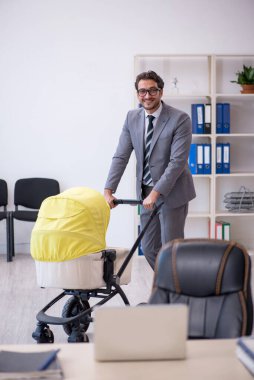 Genç erkek çalışan işyerinde yeni doğan çocuğa bakıyor.