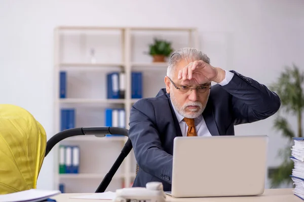 Old male employee looking after new born at workplace — Stock Photo, Image