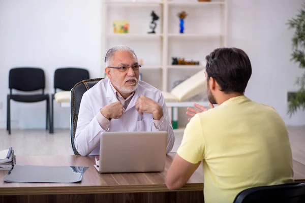 Joven paciente masculino visitando viejo médico masculino —  Fotos de Stock