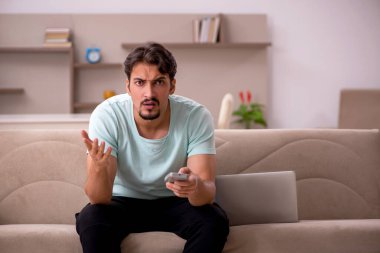 Genç adam evde televizyon izliyor.