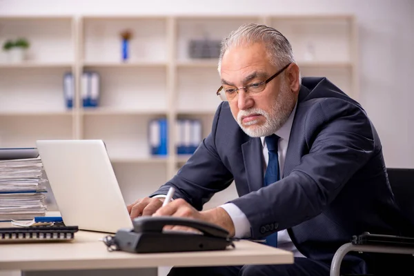 Oude mannelijke werknemer in rolstoel zittend op de werkplek — Stockfoto