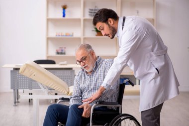 Tekerlekli sandalyedeki yaşlı adam genç erkek doktoru ziyaret ediyor.