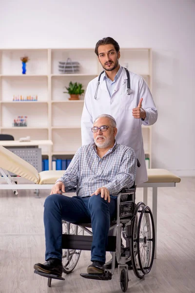 Tekerlekli sandalyedeki yaşlı adam genç erkek doktoru ziyaret ediyor.
