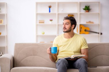 Genç adam salgın sırasında evde kitap okuyor.