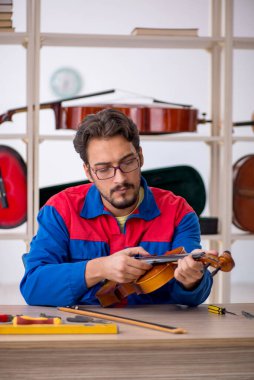 Genç adam atölyede müzik aletlerini tamir ediyor.