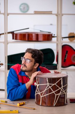 Genç adam atölyede müzik aletlerini tamir ediyor.