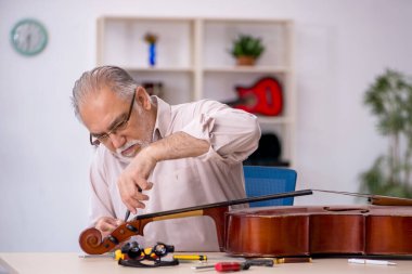 Yaşlı erkek tamirci atölyede müzik aletlerini tamir ediyor.