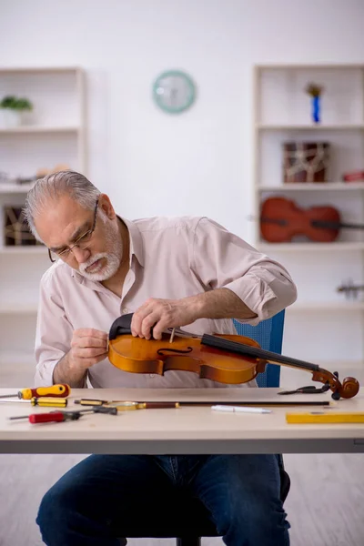 Oude mannelijke reparateur repareert muziekinstrumenten in werkplaats — Stockfoto