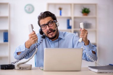 Masasında çalışan genç bir erkek çağrı merkezi operatörü.