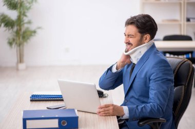 Genç boynu yaralı erkek çalışan ofiste oturuyor.