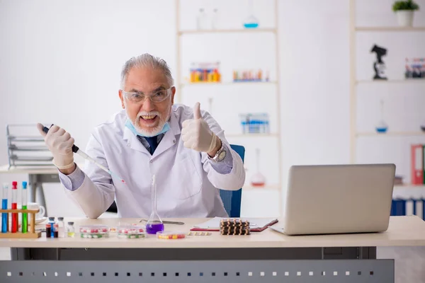 Régi férfi gyógyszerész a gyógyszerszintézis koncepciójában — Stock Fotó