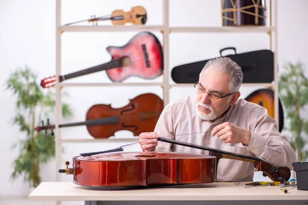 Oude mannelijke reparateur repareert muziekinstrumenten op het werk — Stockfoto