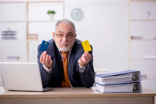 Homem velho empregado segurando cartão de crédito no escritório — Fotografia de Stock