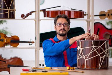 Genç adam atölyede müzik aletlerini tamir ediyor.