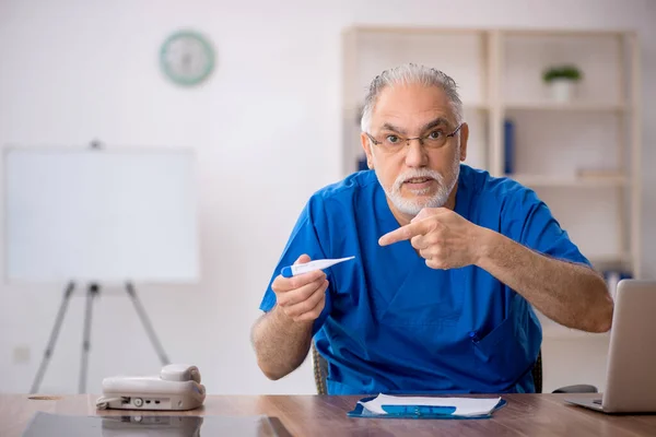 Klinikte termometre tutan yaşlı bir erkek doktor. — Stok fotoğraf