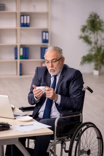 Oude mannelijke werknemer in rolstoel zittend op de werkplek — Stockfoto