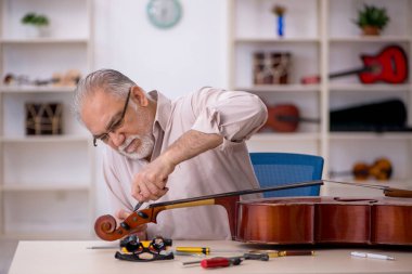 Yaşlı erkek tamirci atölyede müzik aletlerini tamir ediyor.
