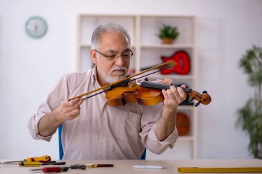 Yaşlı erkek tamirci atölyede müzik aletlerini tamir ediyor.