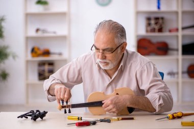 Yaşlı erkek tamirci atölyede müzik aletlerini tamir ediyor.