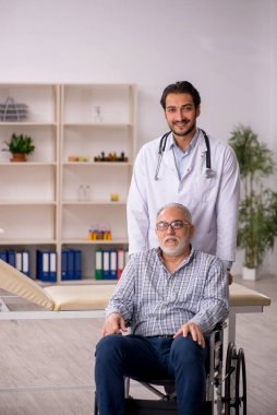 Tekerlekli sandalyedeki yaşlı adam genç erkek doktoru ziyaret ediyor.