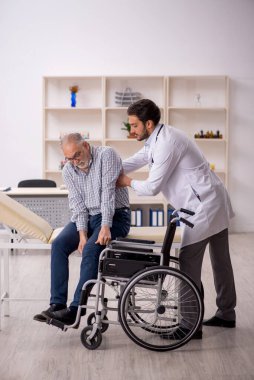 Tekerlekli sandalyedeki yaşlı adam genç erkek doktoru ziyaret ediyor.