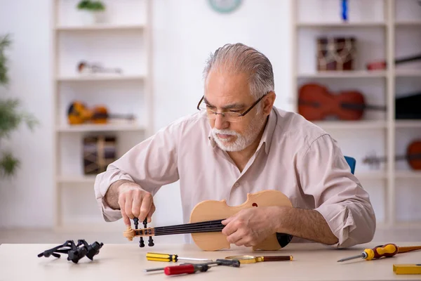 Oude mannelijke reparateur repareert muziekinstrumenten in werkplaats — Stockfoto