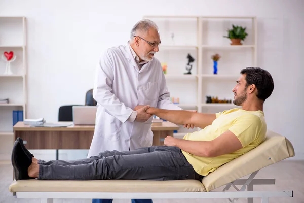 Genç erkek hasta yaşlı erkek doktor masörünü ziyaret ediyor. — Stok fotoğraf