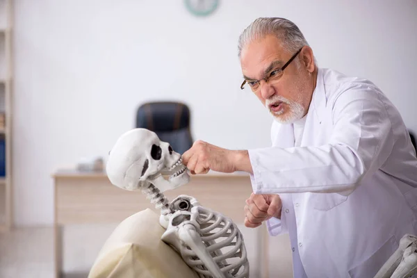 Vecchio medico maschio con scheletro in clinica — Foto Stock
