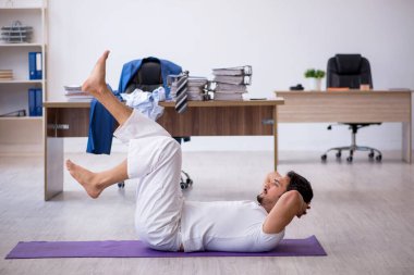 Genç erkek çalışan ofiste spor egzersizleri yapıyor.