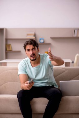 Genç adam evde televizyon izliyor.