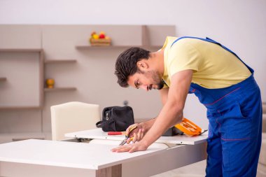 Genç erkek marangoz evdeki masayı onarıyor.