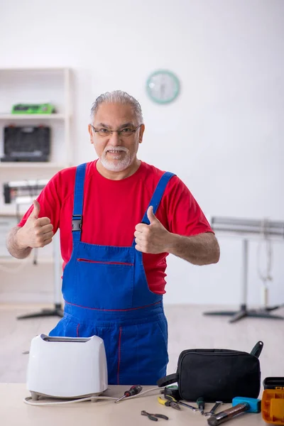 Oude reparateur repareert broodrooster in werkplaats — Stockfoto