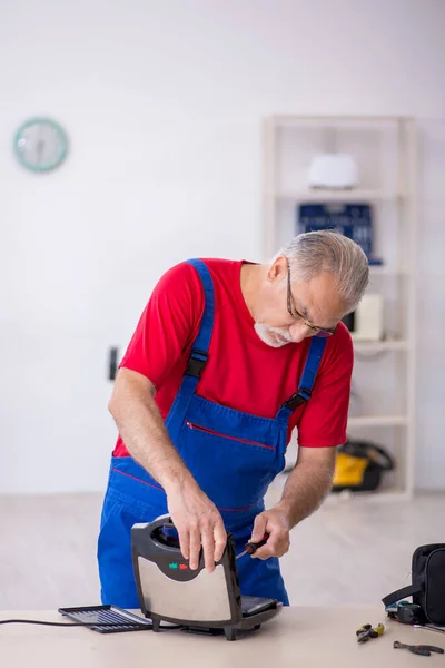 Oude reparateur repareert sandwichmachine in werkplaats — Stockfoto