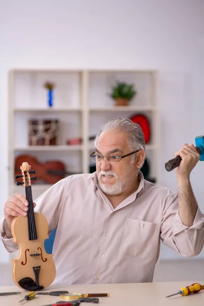 Alter Mann repariert Musikinstrumente in Werkstatt — Stockfoto
