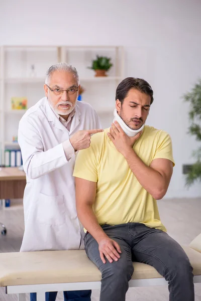 Junge männliche Nackenverletzung Patient besucht alten männlichen Arzt — Stockfoto