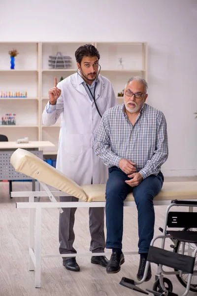 Anciano en silla de ruedas visitando al joven médico masculino —  Fotos de Stock