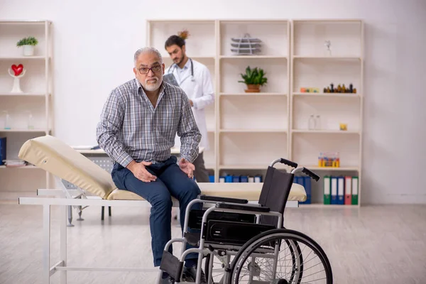 Vecchio in sedia a rotelle visita giovane medico maschio — Foto Stock