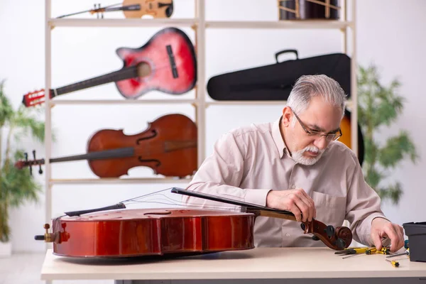 Oude mannelijke reparateur repareert muziekinstrumenten op het werk — Stockfoto