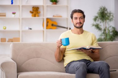 Genç adam salgın sırasında evde kitap okuyor.