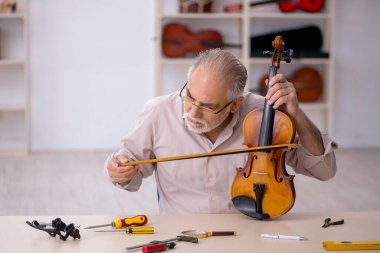 Yaşlı erkek tamirci atölyede müzik aletlerini tamir ediyor.