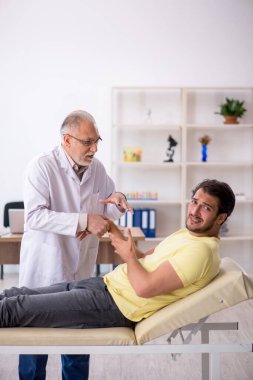 Genç erkek hasta yaşlı erkek doktor masörünü ziyaret ediyor.