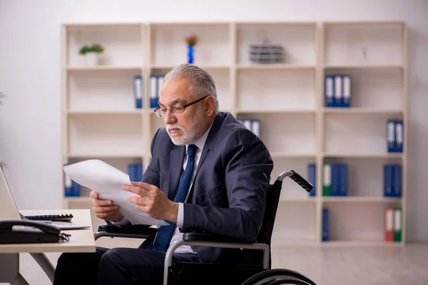 Stary męski pracownik na wózku inwalidzkim siedzi w miejscu pracy — Zdjęcie stockowe
