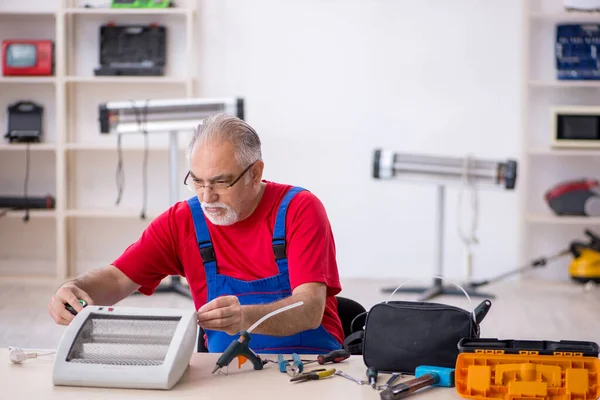 Old repairman repairing heater at workshop