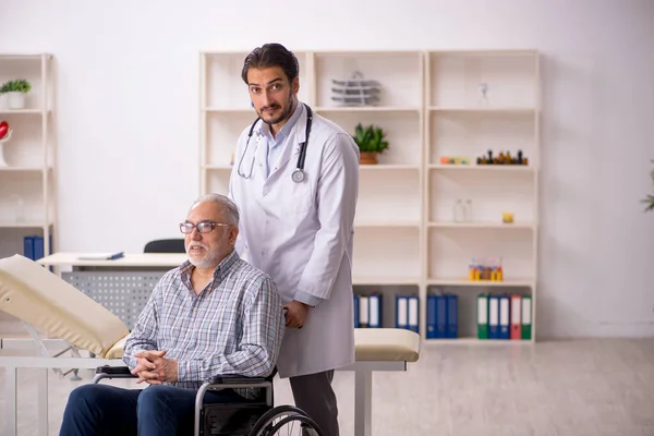 Anciano en silla de ruedas visitando al joven médico masculino — Foto de Stock